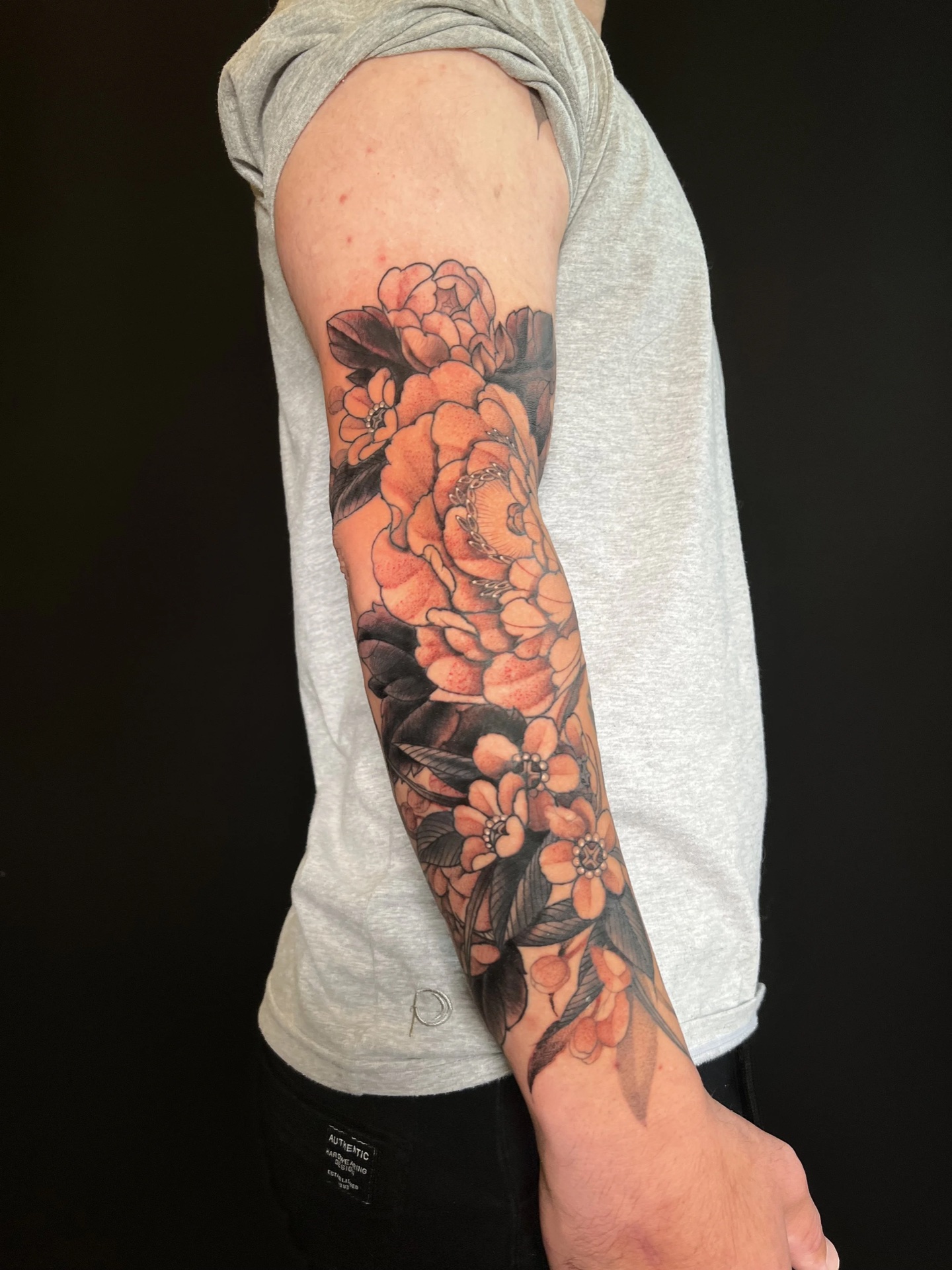 Black and grey and orange peony forearm tattoo by Levi Taylor